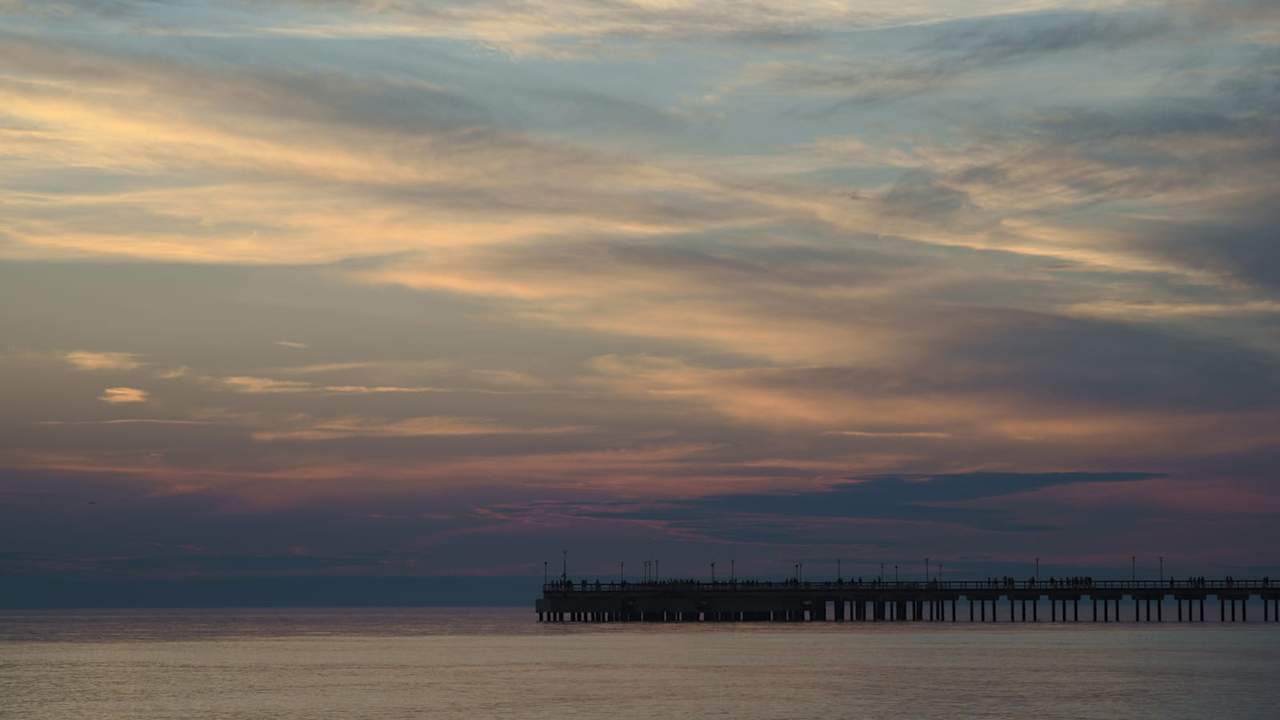 Saulėlydžio debesys virš ramios jūros ir Palangos tilto siluetas horizonte