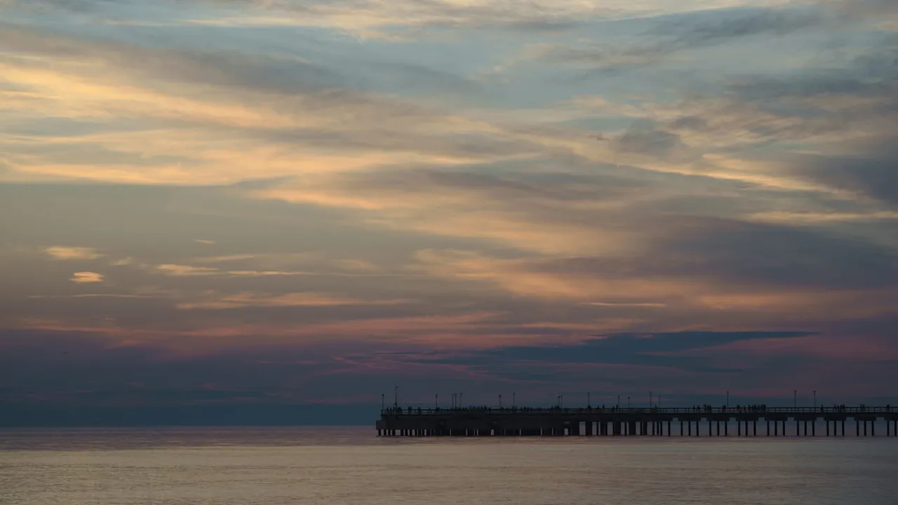 Saulėlydžio debesys virš ramios jūros ir Palangos tilto siluetas horizonte
