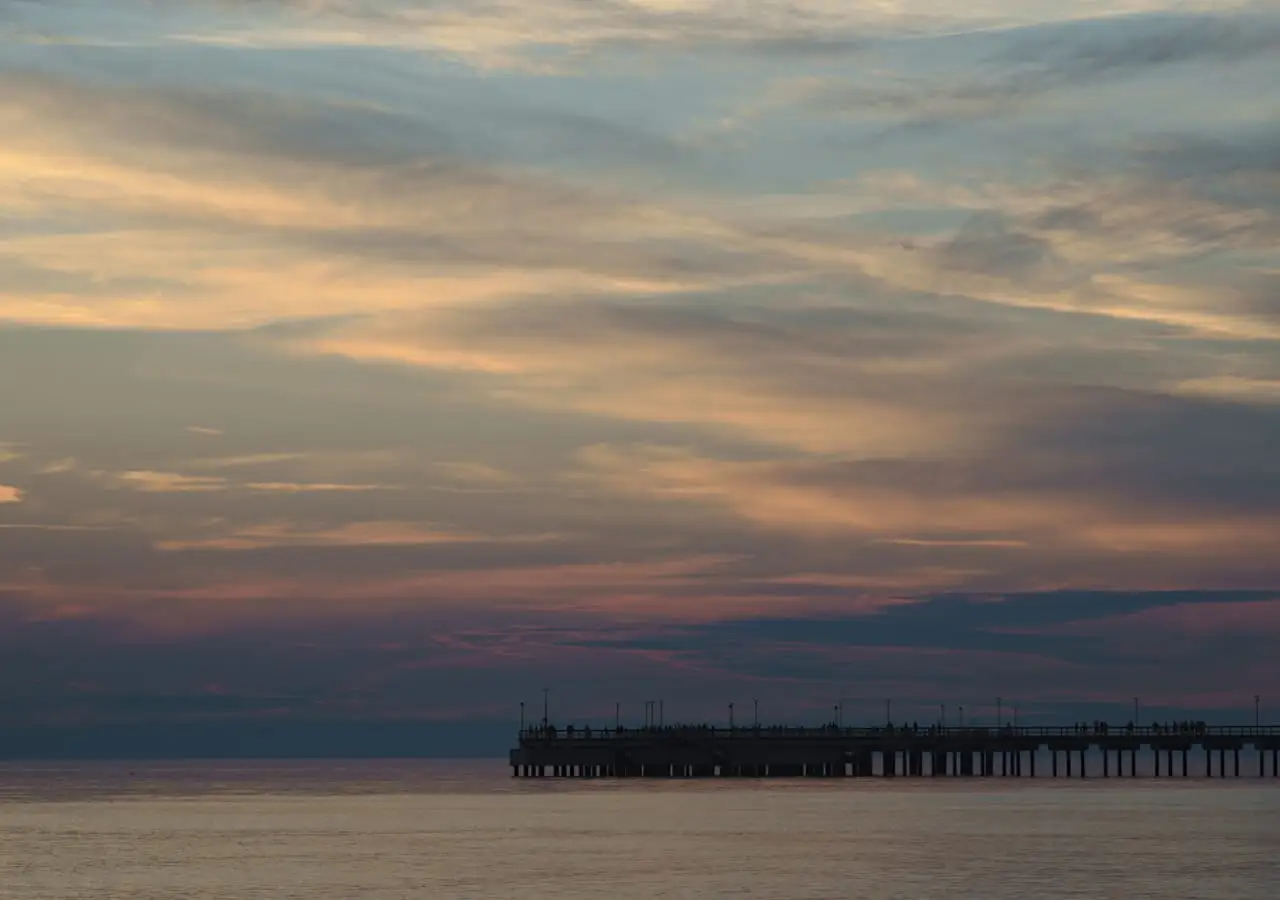 Saulėlydžio debesys virš ramios jūros ir Palangos tilto siluetas horizonte