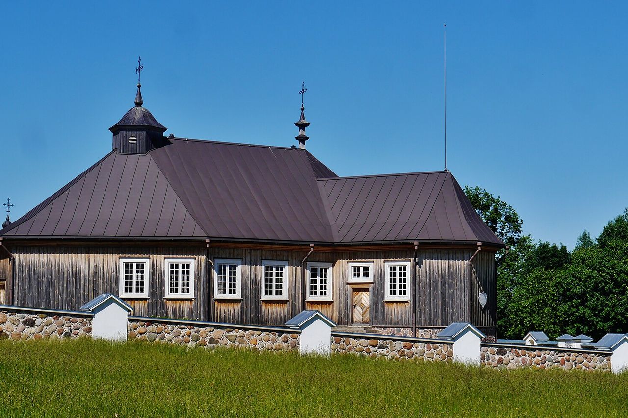 Medinė bažnyčia su rudu stogu už akmeninės tvoros muziejaus miestelyje, giedras dangus