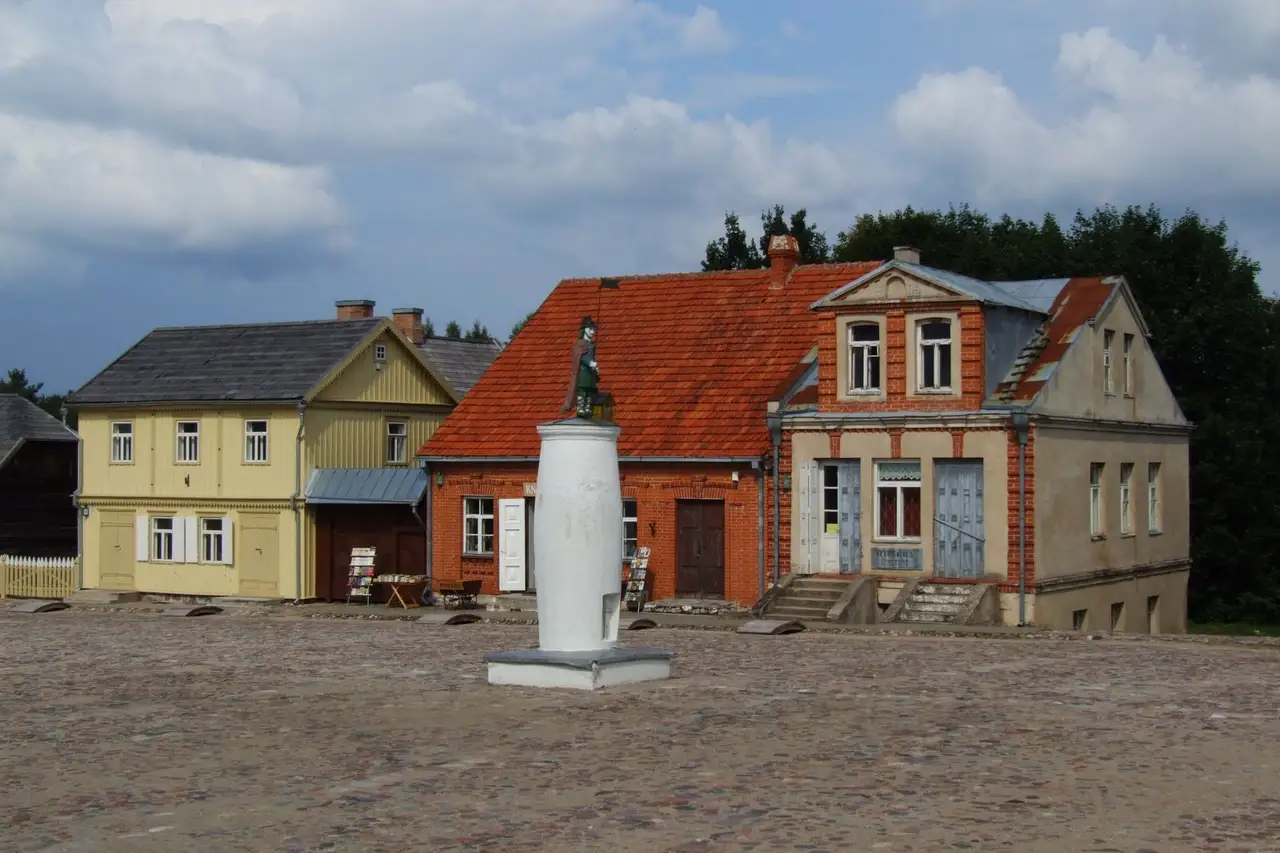 Senoviniai mediniai ir plytų namai su skulptūra aikštės viduryje Rumšiškių muziejuje