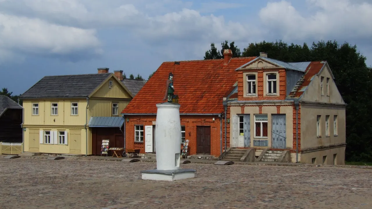 Senoviniai mediniai ir plytų namai su skulptūra aikštės viduryje Rumšiškių muziejuje