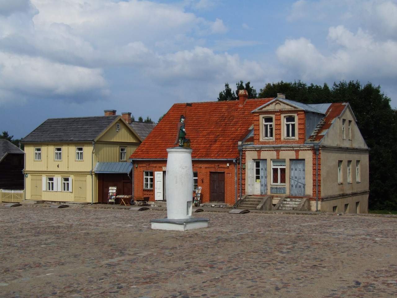 Senoviniai mediniai ir plytų namai su skulptūra aikštės viduryje Rumšiškių muziejuje