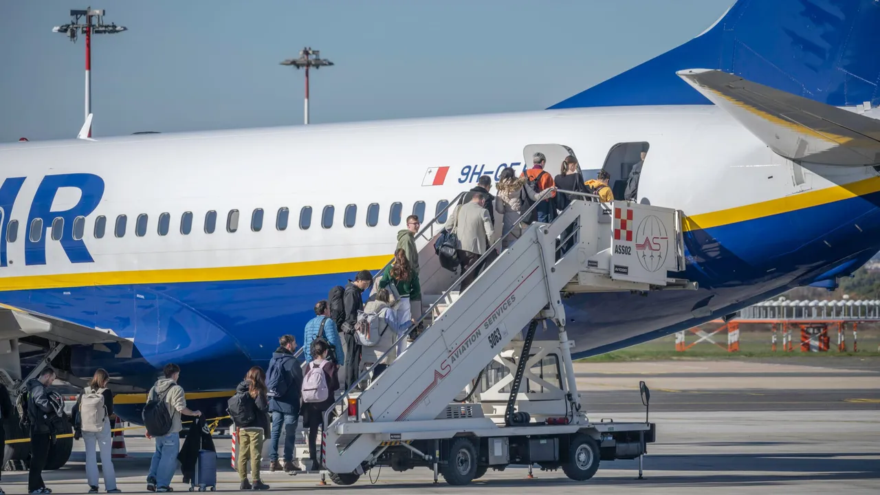 Keleiviai su kuprinėmis eina laiptais į Ryanair lėktuvą oro uosto aikštelėje