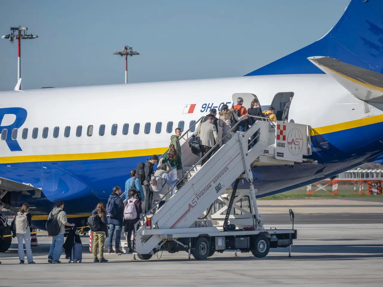 Keleiviai su kuprinėmis eina laiptais į Ryanair lėktuvą oro uosto aikštelėje