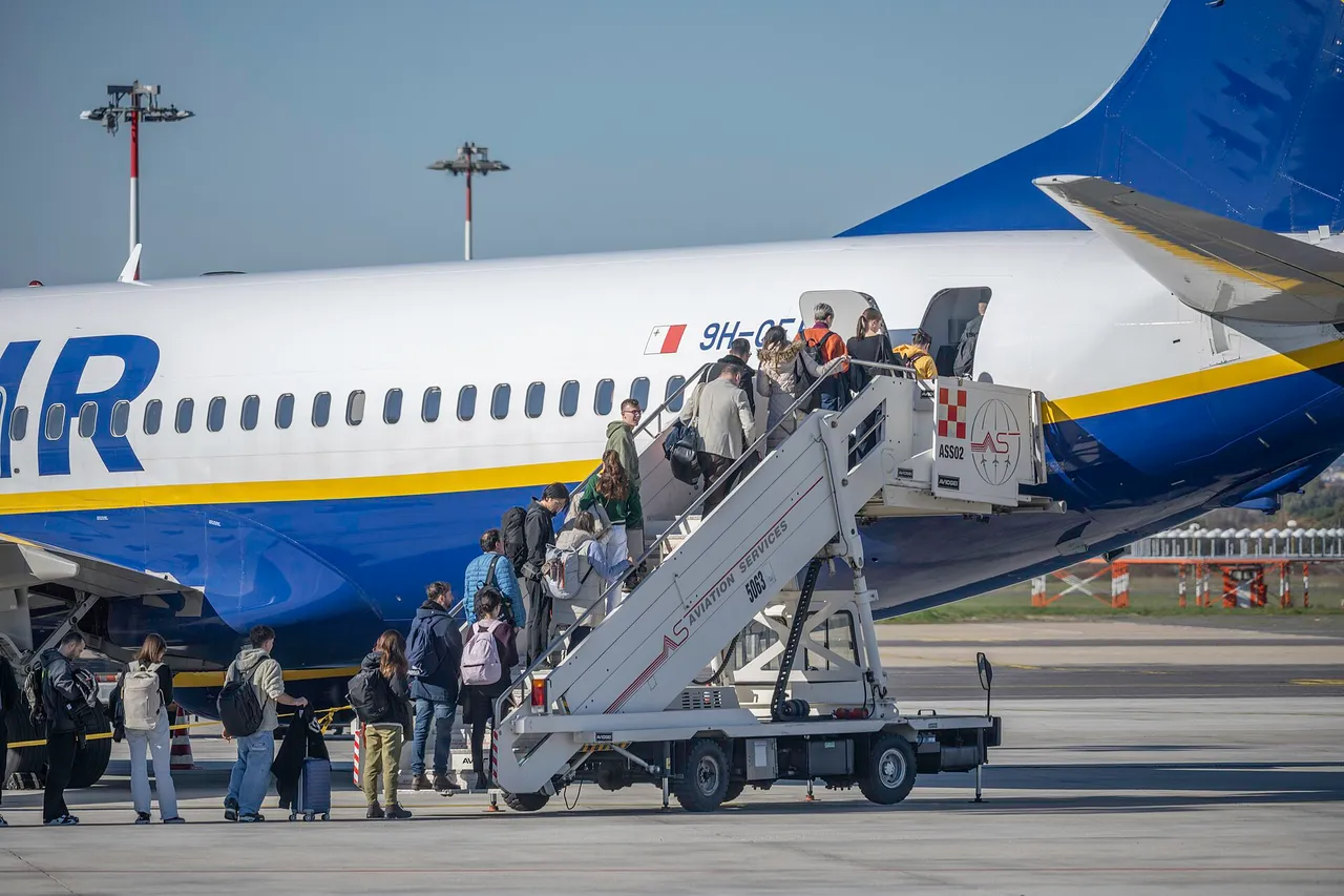 Keleiviai su kuprinėmis ir lagaminu eina laipteliais į Ryanair lėktuvo galines duris