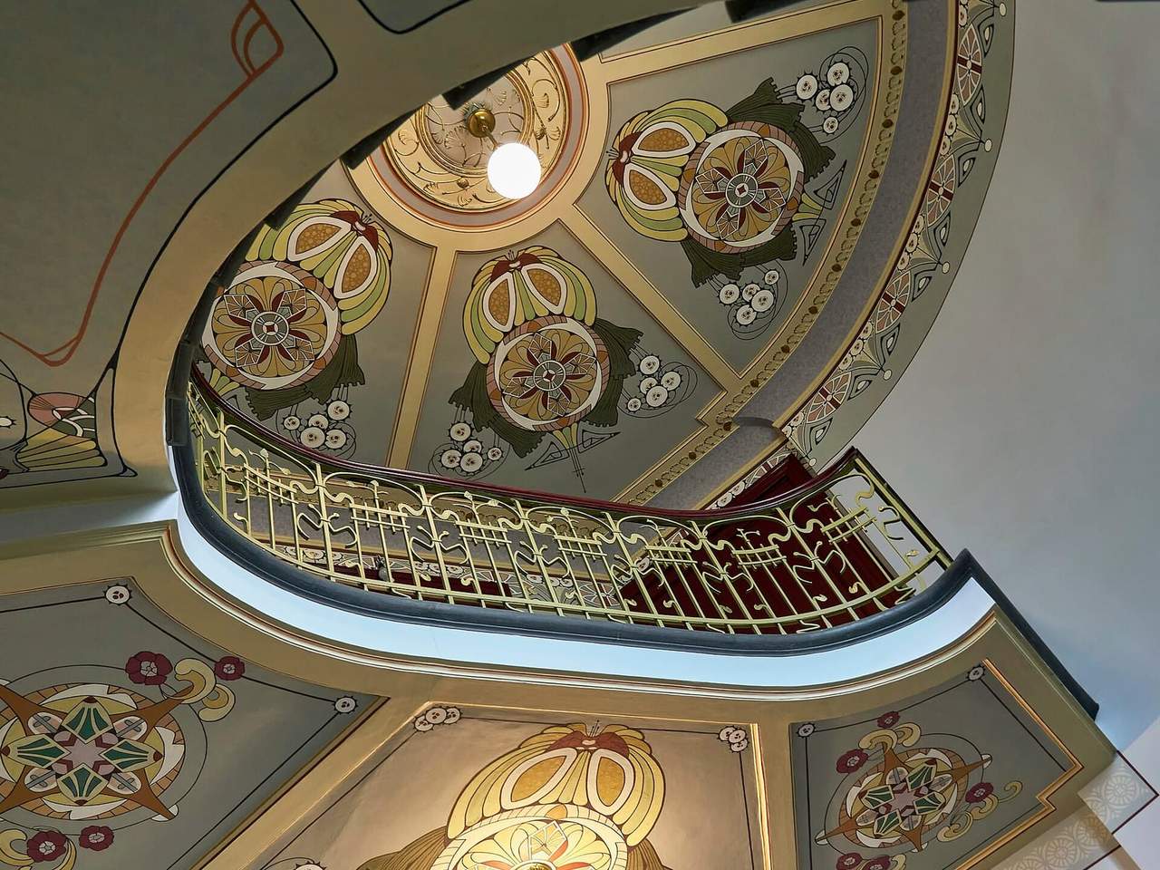 Dekoruotas Art Nouveau laiptinės skliautas su aukso spalvos turėklais ir lempa