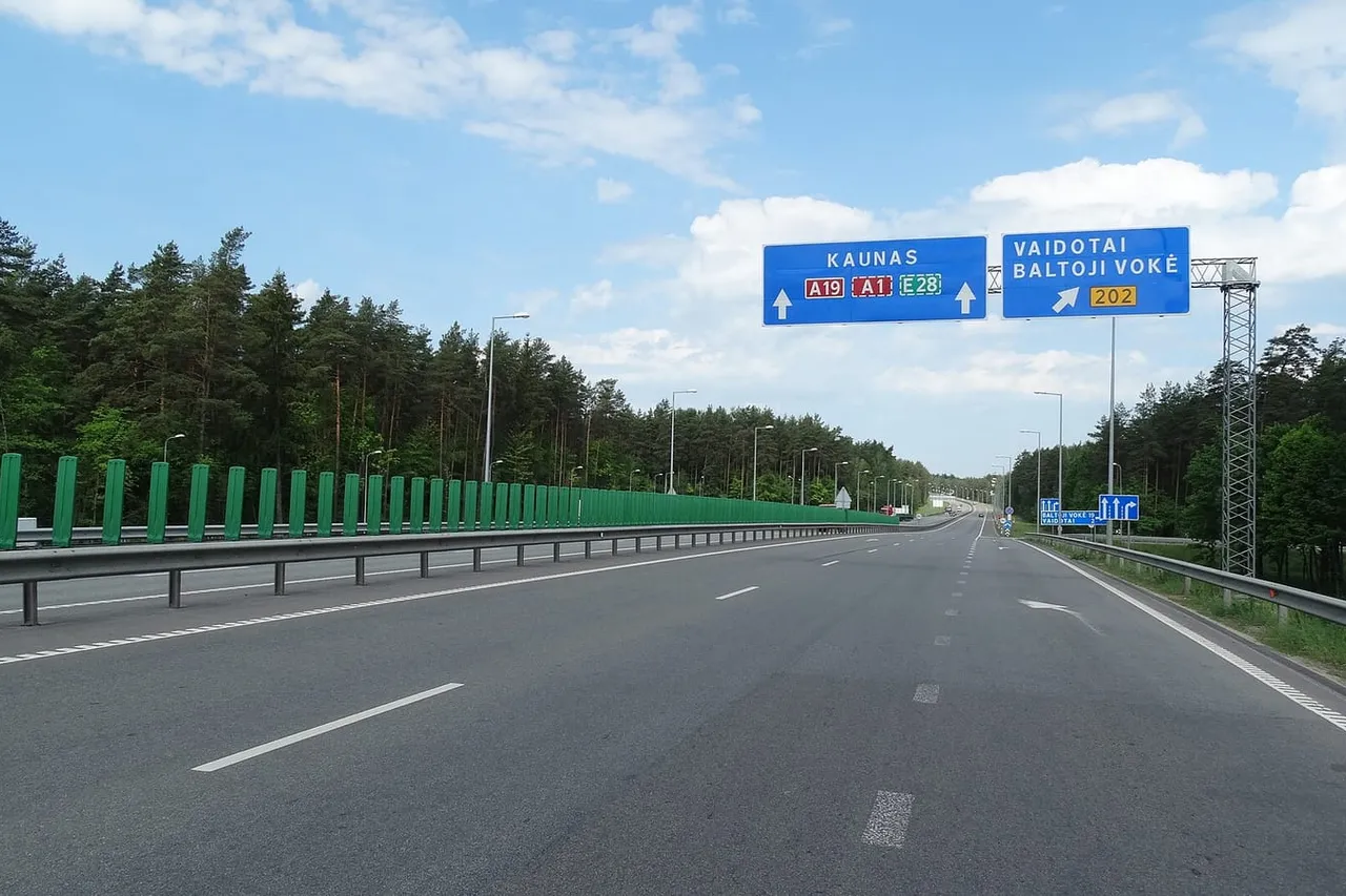 Tuščias greitkelis A19 su mėlynu ženklu į Kauną tarp pušynų Vilniaus apylinkėse