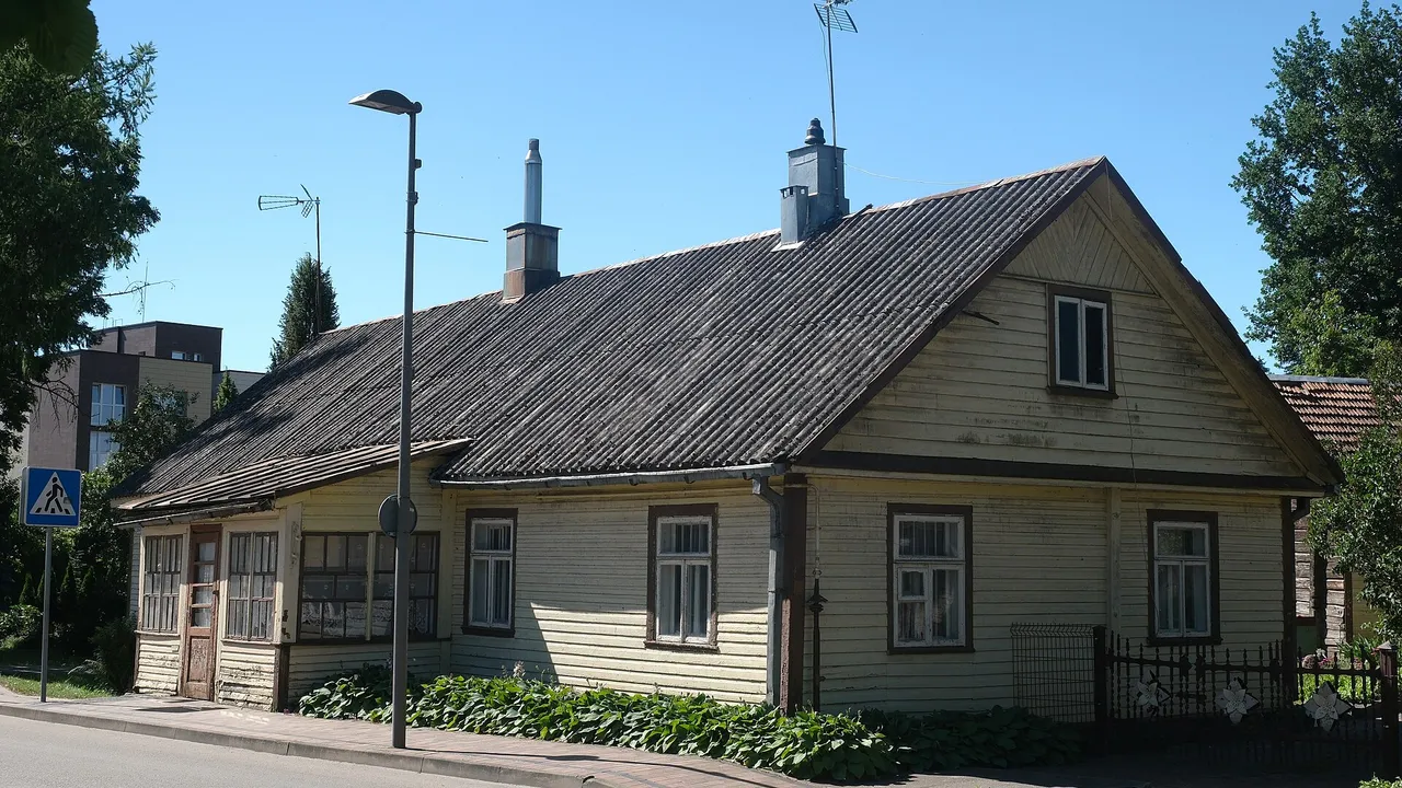 Geltonas medinis namas su pilku stogu Birštono gatvėje giedrą vasaros dieną