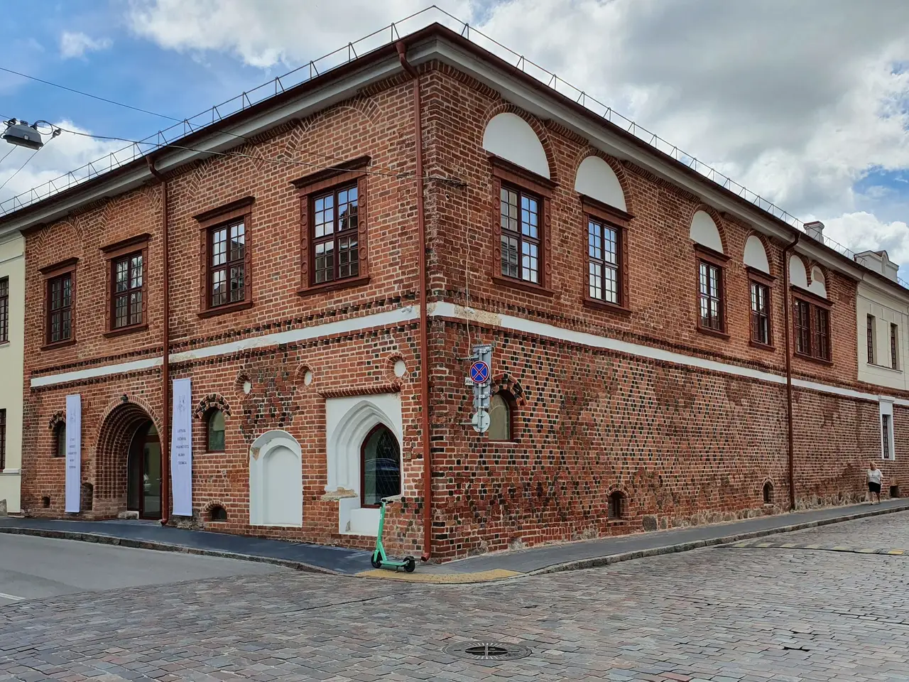 Raudonų plytų pastatas Kauno senamiestyje, matomas nuo gatvės kampo, grįsta gatvė