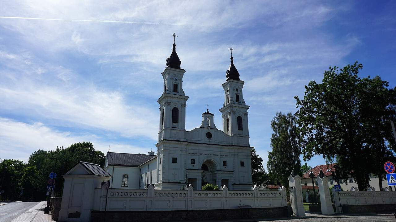 Dviejų bokštų baltas Marijampolės Šv. arkangelo Mykolo bazilikos fasadas ir balta šventoriaus tvora
