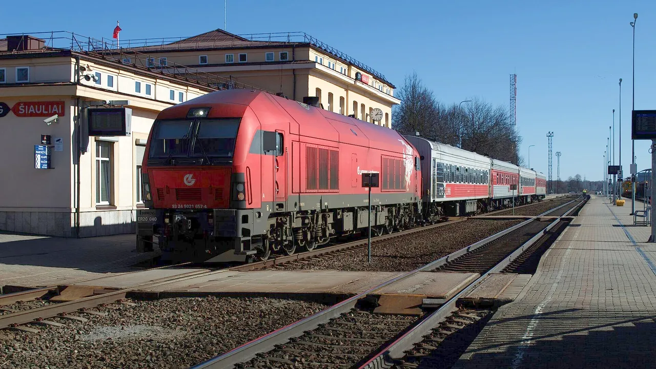 Raudonas lokomotyvas su keleiviniais vagonais Šiaulių geležinkelio stotyje giedrą dieną