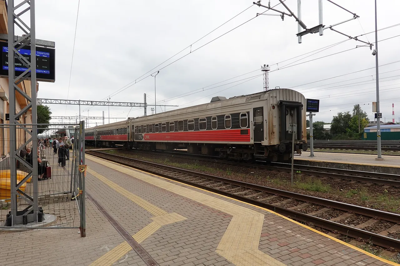 Šiaulių stoties peronas su užrašu „Šiauliai“ ir stovinčiu raudonai baltu traukiniu