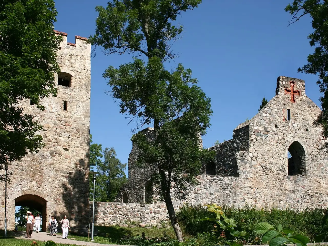 Siguldos pilies akmeniniai griuvėsiai su bokštu ir arka, pro ją eina keli žmonės