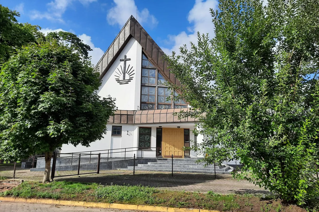 Moderni balta Šilutės bažnyčia trikampe fasado forma, aplink medžiai