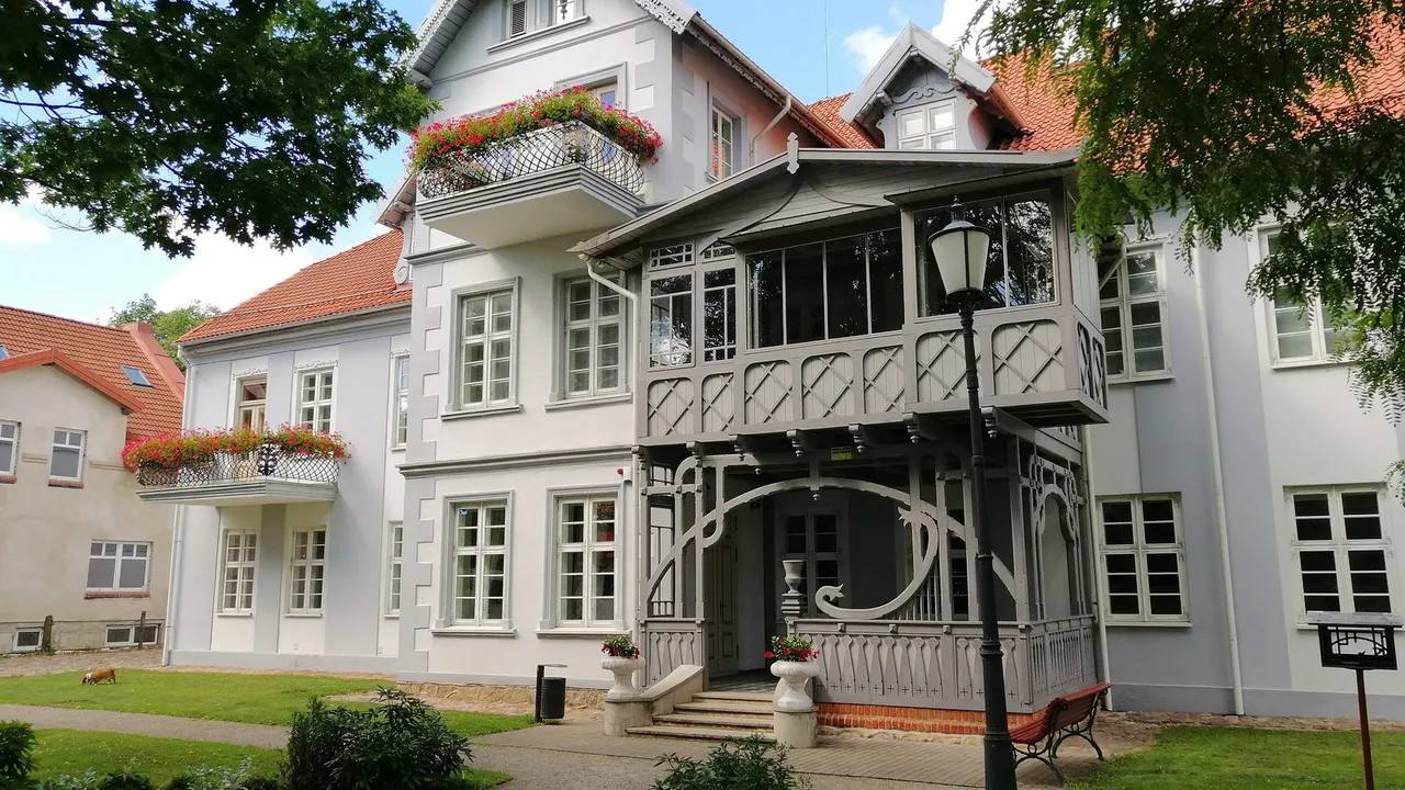 Šilutės dvaro rūmų įėjimas su medine veranda, balkonais su gėlėmis ir gėlynu priekyje