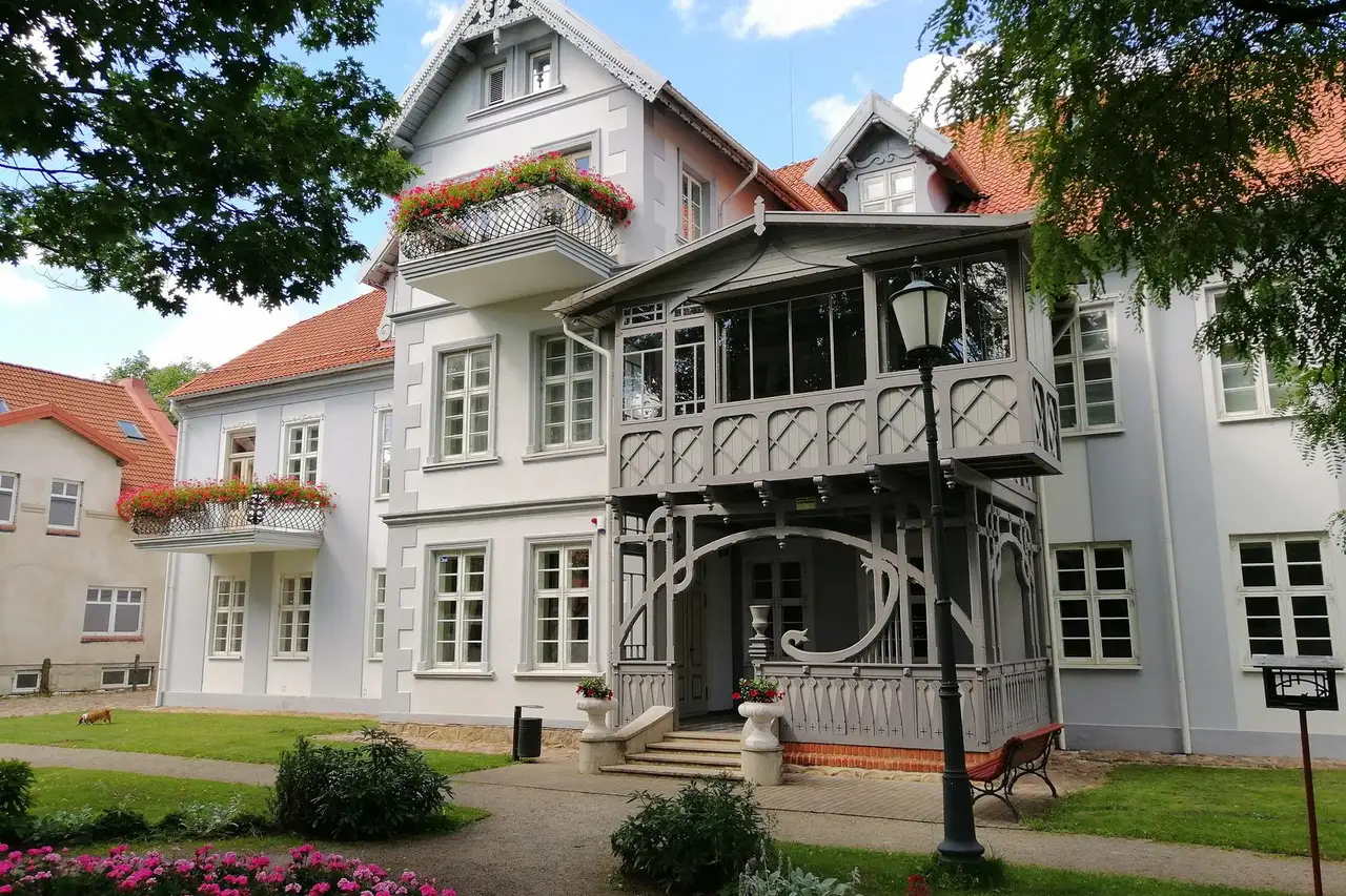 Šilutės dvaro rūmų įėjimas su medine veranda, balkonais su gėlėmis ir gėlynu priekyje