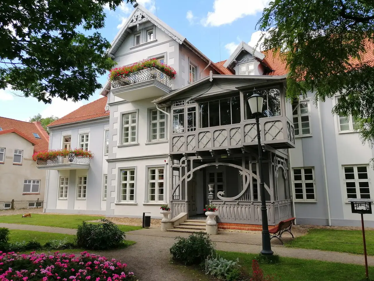 Šilutės dvaro rūmų įėjimas su medine veranda, balkonais su gėlėmis ir gėlynu priekyje