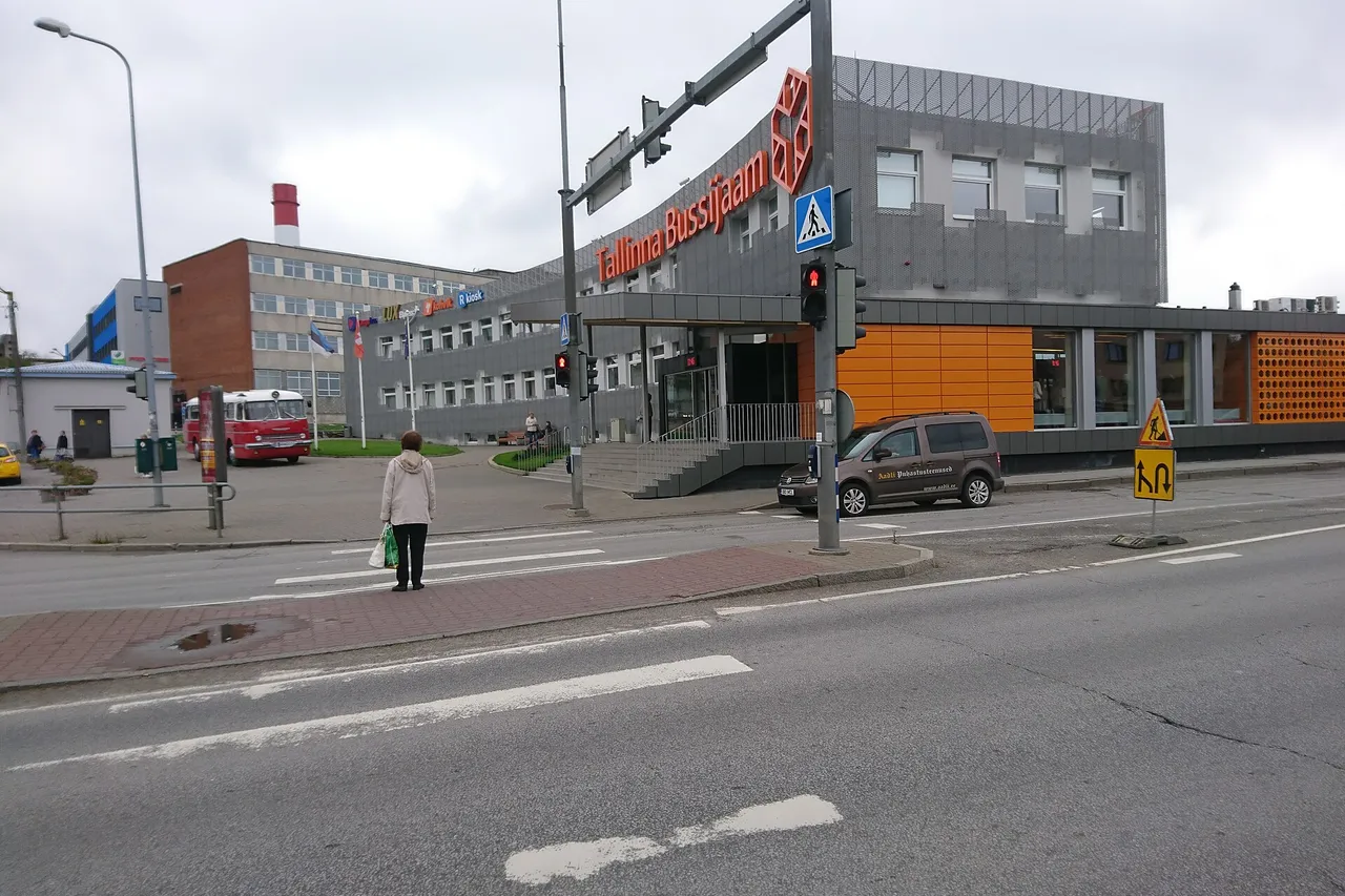 Talino autobusų stoties pastatas su oranžiniu užrašu, kampuota fasado danga ir raudonu senoviniu autobusu