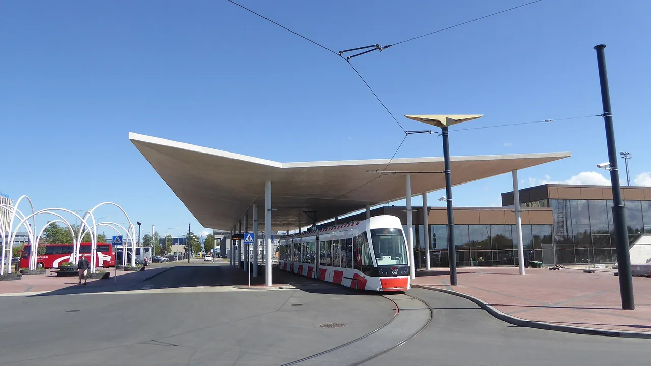 Baltai raudonas Talino tramvajus Nr. 4 pasukimo kilpoje po plačiu stogu prie oro uosto, šalia stovi autobusai