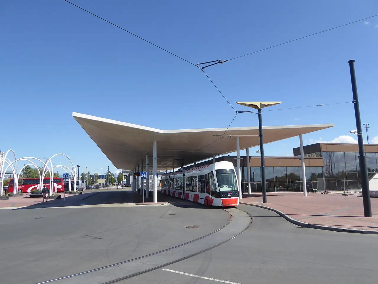 Baltai raudonas Talino tramvajus Nr. 4 pasukimo kilpoje po plačiu stogu prie oro uosto, šalia stovi autobusai