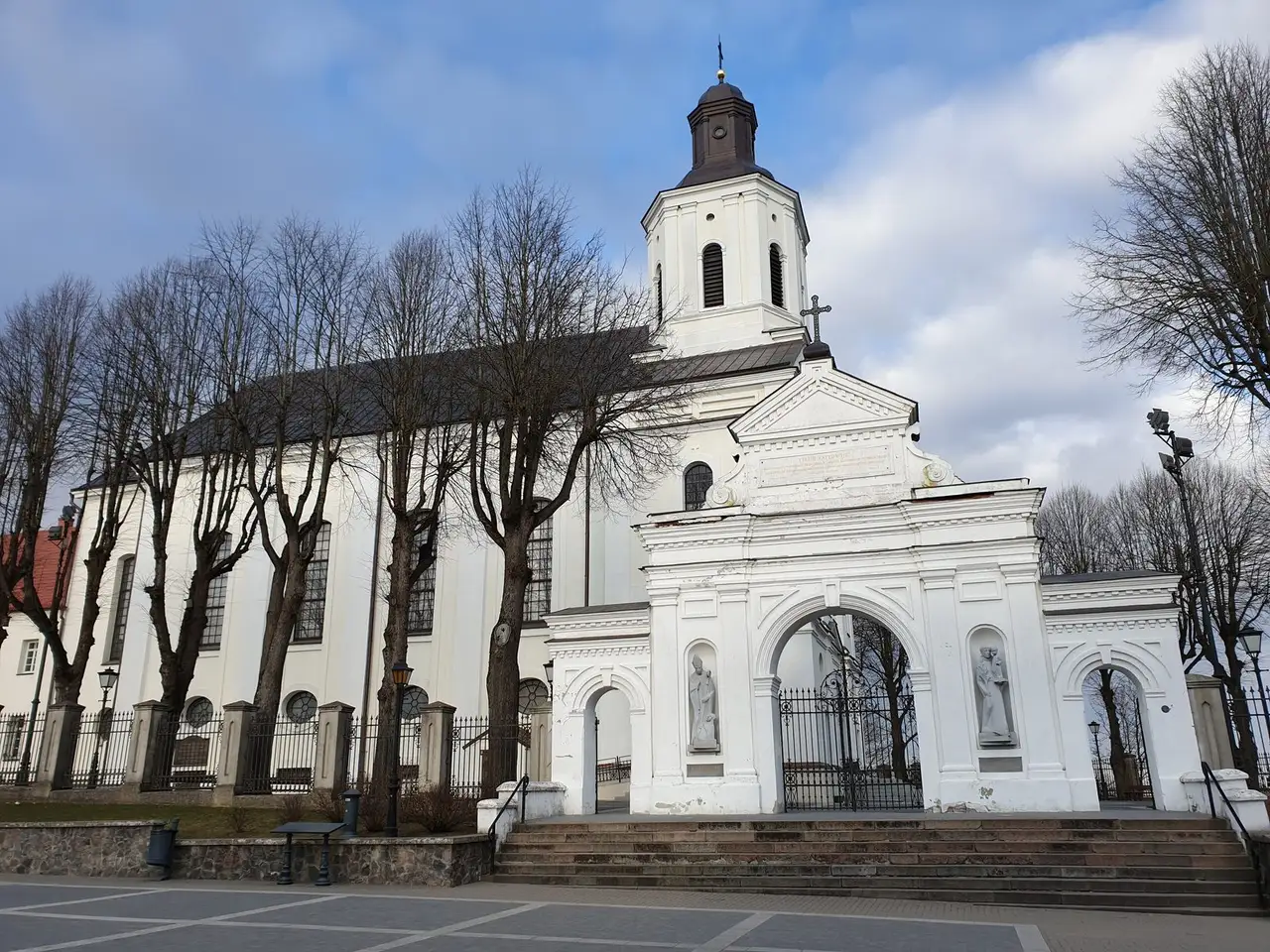 Balta Telšių Šv. Antano Paduviečio katedra su šventoriaus vartais ir plikais medžiais priekyje