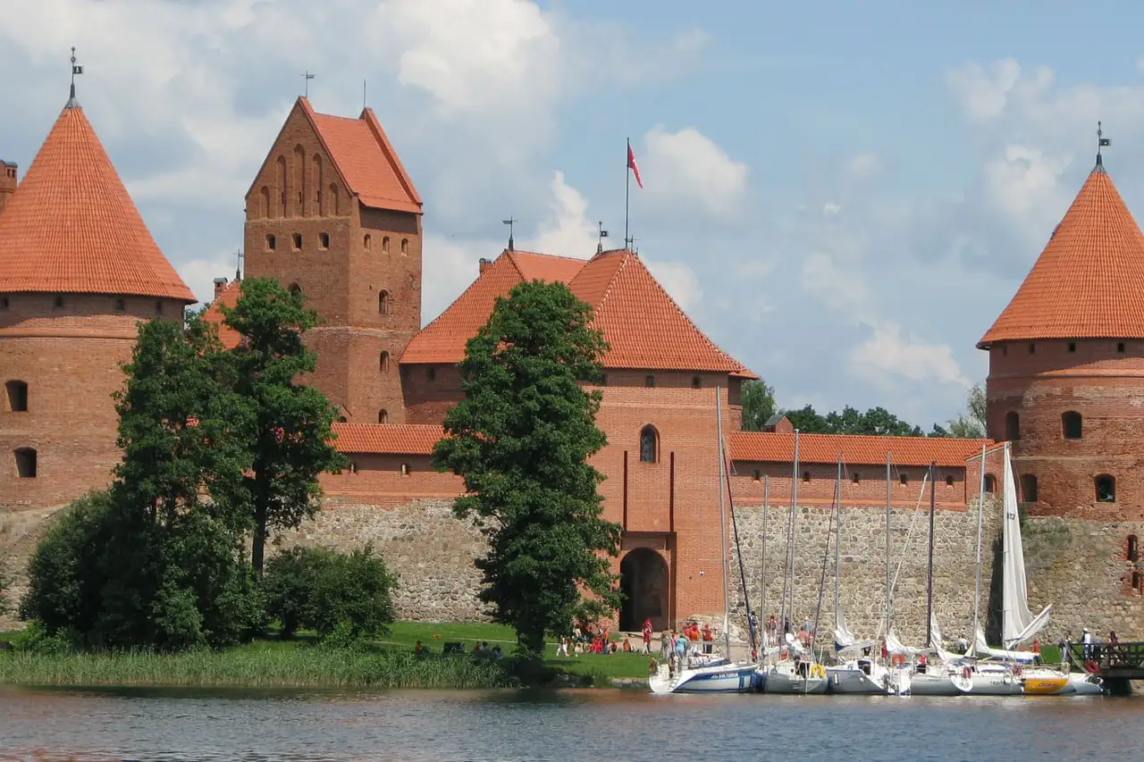 Raudonų plytų Trakų Salos pilies bokštai prie ežero, priekyje prišvartuotos jachtos