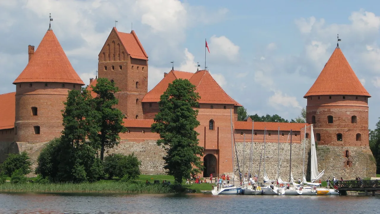 Raudonų plytų Trakų Salos pilies bokštai prie ežero, priekyje prišvartuotos jachtos