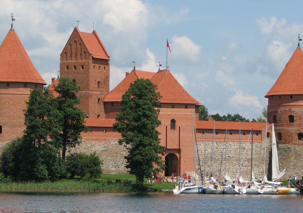 Raudonų plytų Trakų Salos pilies bokštai prie ežero, priekyje prišvartuotos jachtos