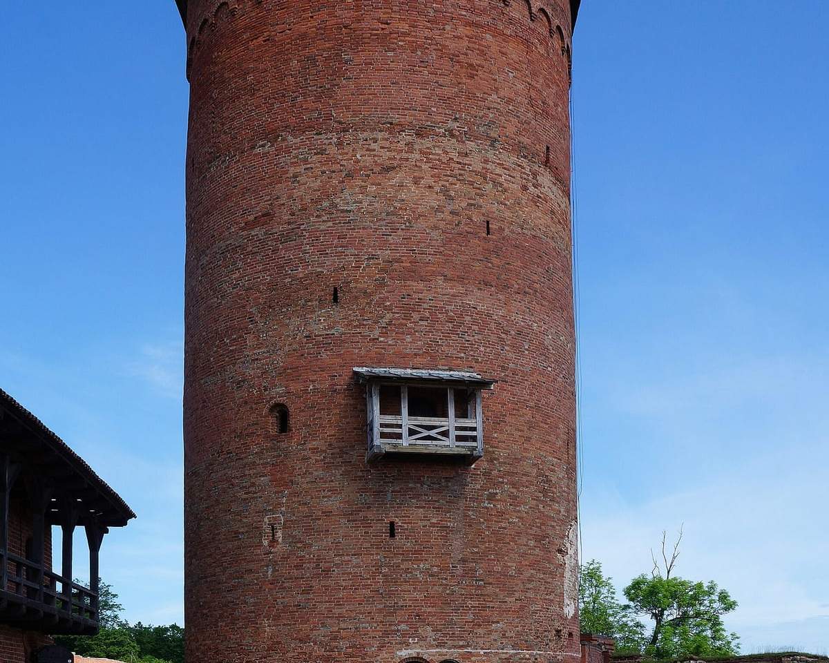 Raudonų plytų Turaidos pilies bokštas su balkonėliu, priekyje žvyruotas kiemas