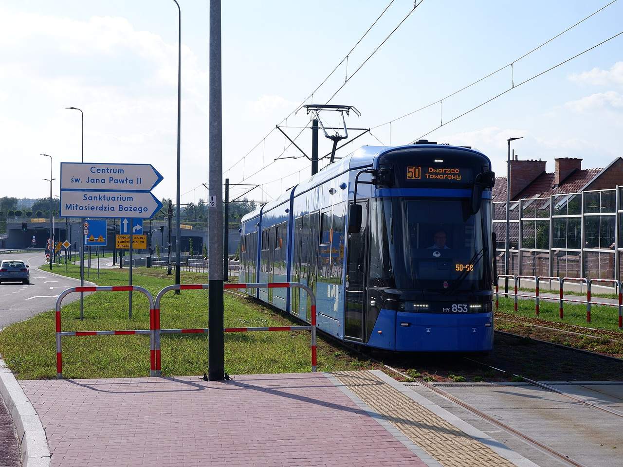 Mėlynas Krokuvos tramvajus 50 linijoje važiuoja pievos juosta tarp kelio ir namų