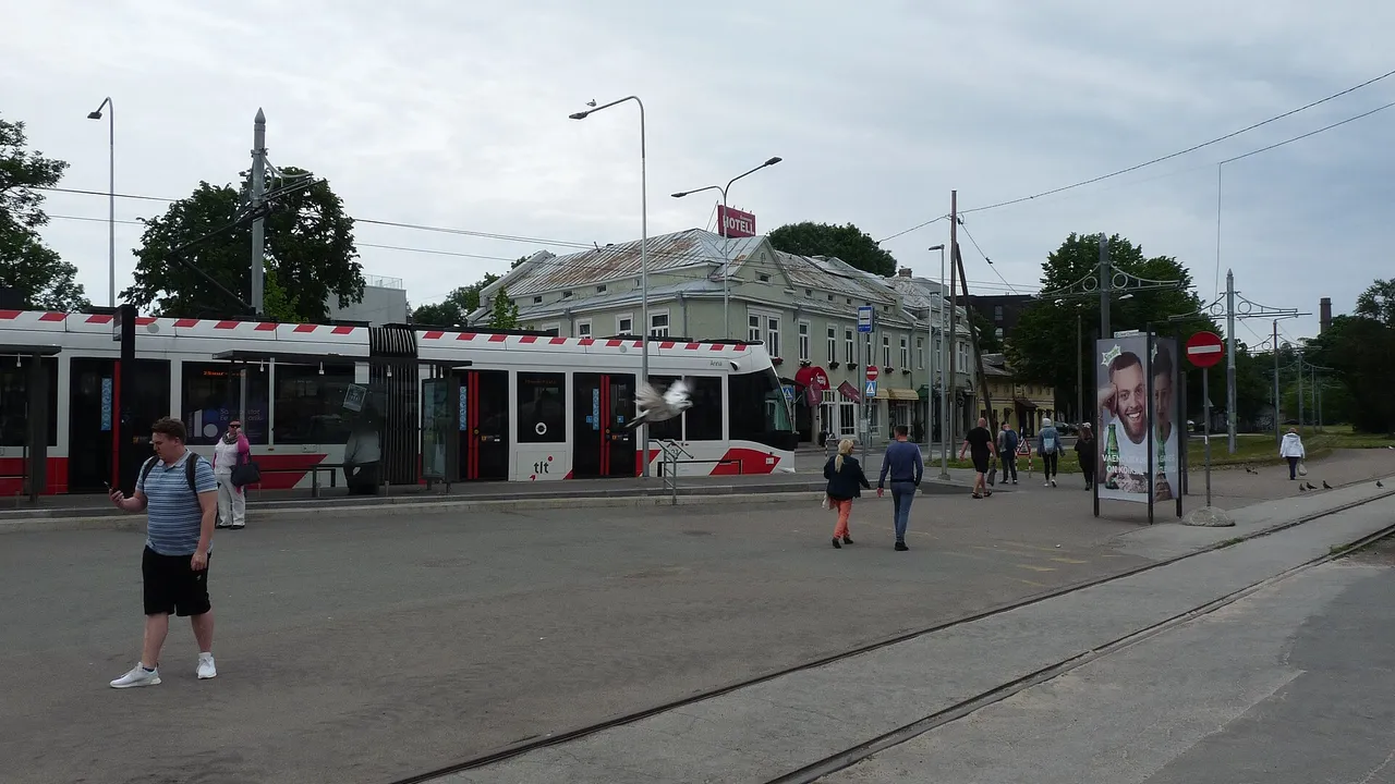 Raudonai baltas Talino tramvajas stotelėje, šalia pėstieji ir žalias pastatas