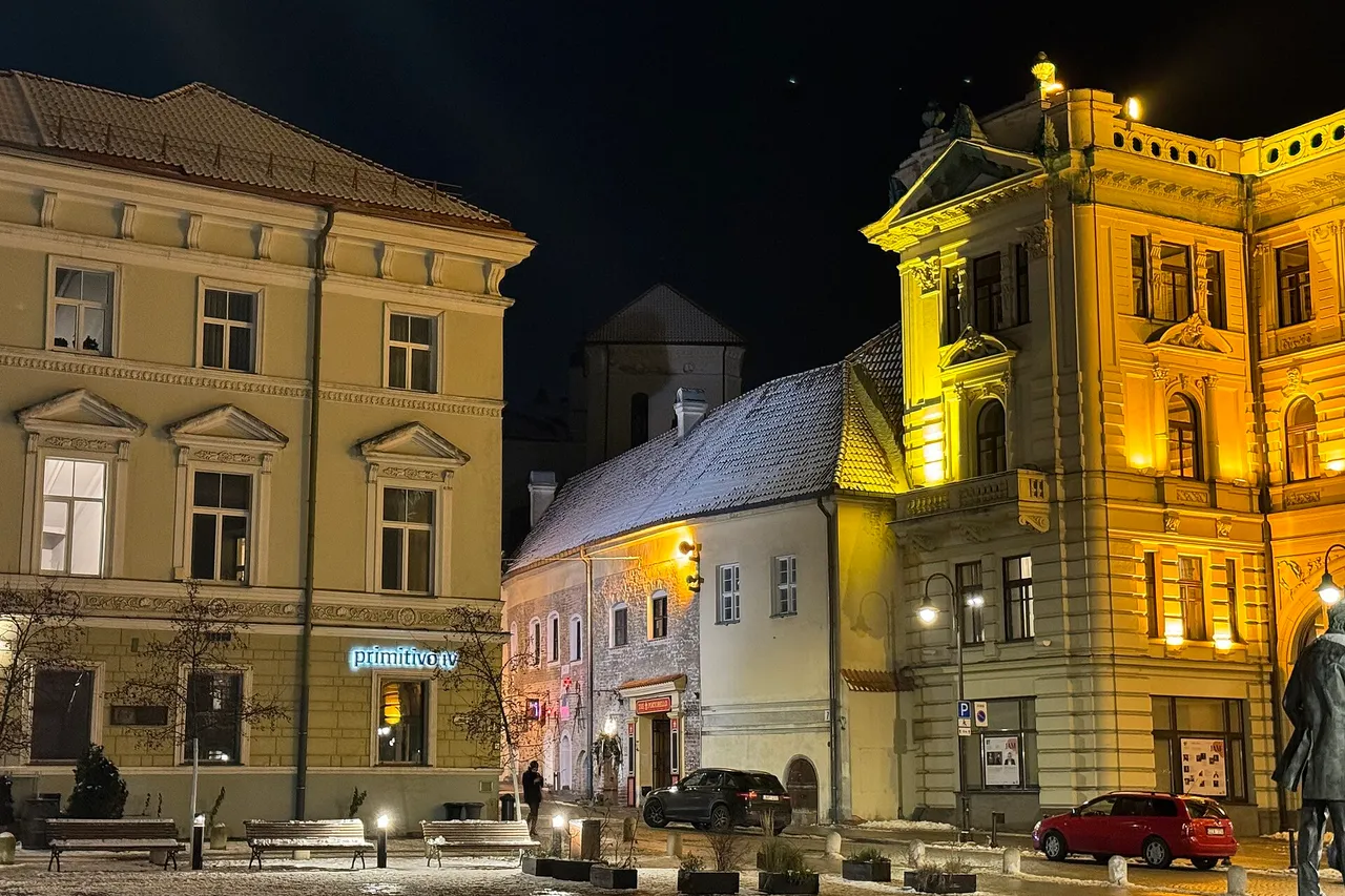 Vilniaus senamiesčio pastatai vakare su šviečiančiais languose ir sniegu ant stogo