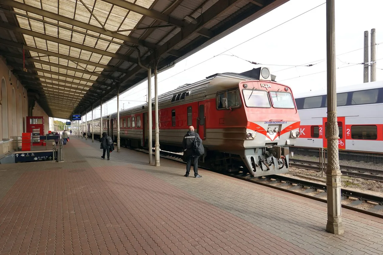 Raudonas dyzelinis traukinys Vilniaus geležinkelio stoties perone po stogine, laukia keleiviai
