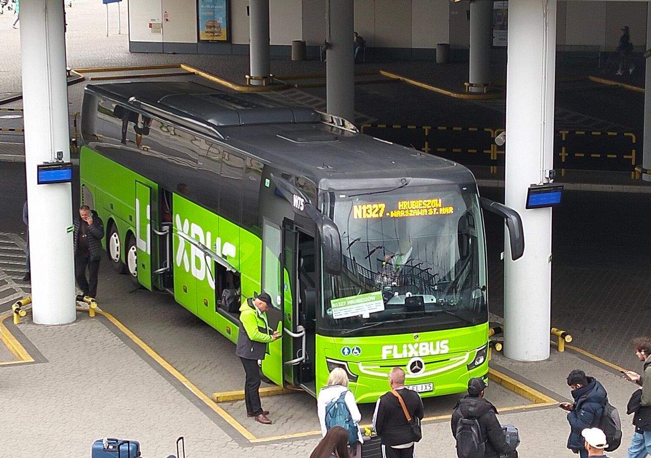 Žalias „FlixBus“ autobusas stovi stotyje po stogine, aplink laukia keleiviai su kuprinėmis