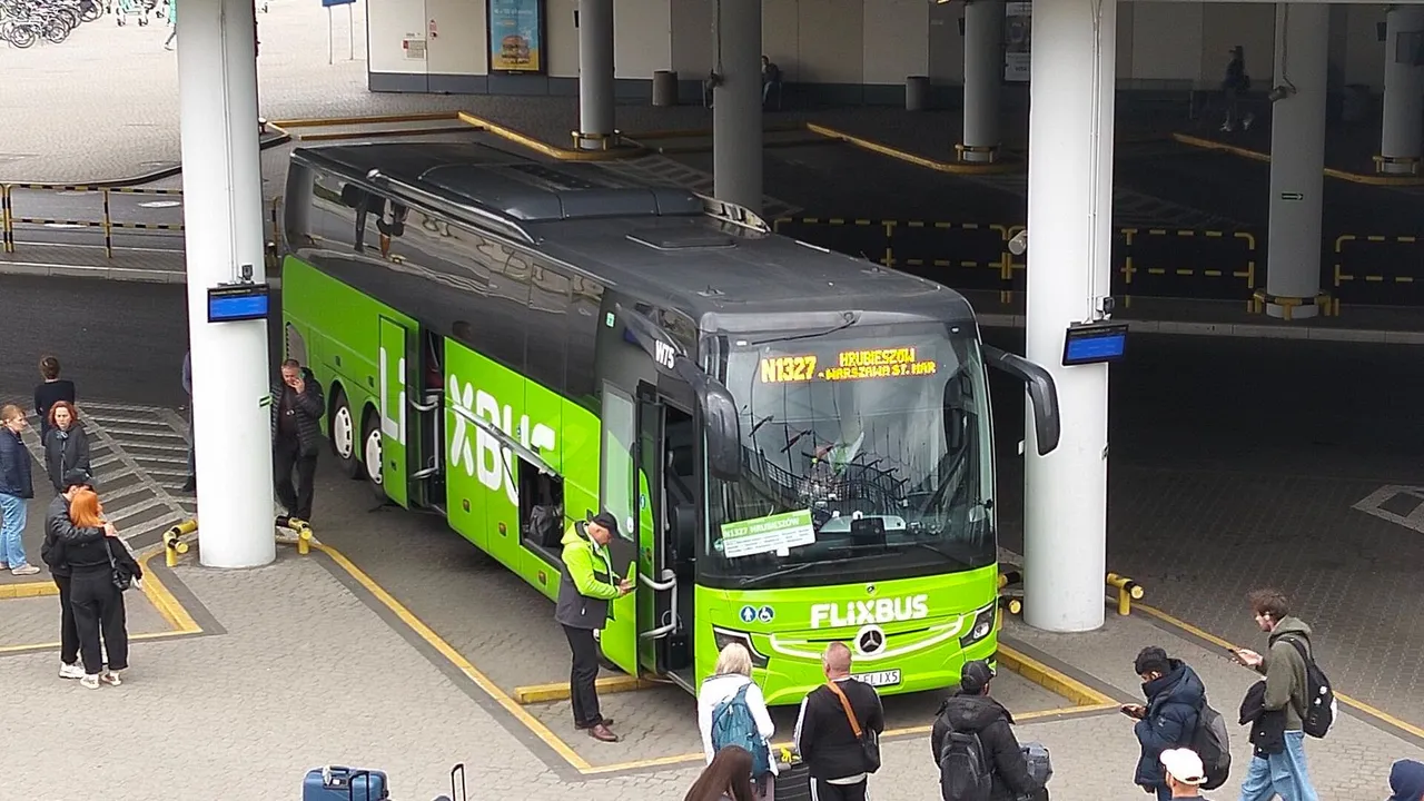 Žalias „FlixBus“ autobusas stovi stotyje po stogine, aplink laukia keleiviai su kuprinėmis