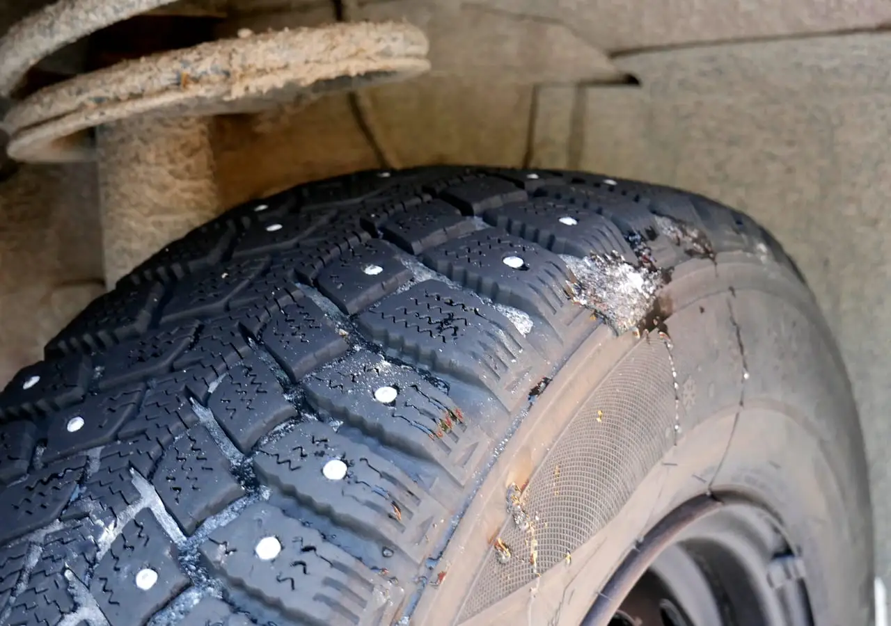 Dygliuota žieminė padanga automobilio rato arkoje, matomi metaliniai dygliai ir protektoriaus raštas