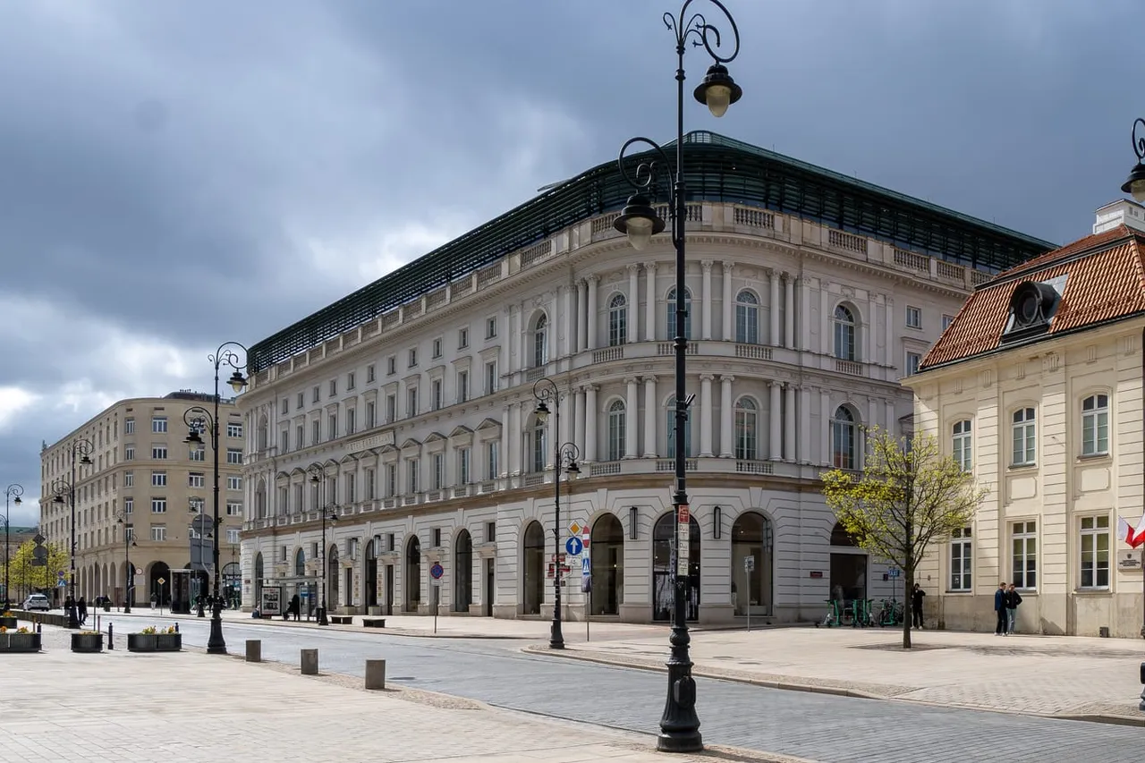 Krakowskie Przedmieście gatvė Varšuvoje su žibintais ir šviesiais istoriniais pastatais po debesuotu dangumi