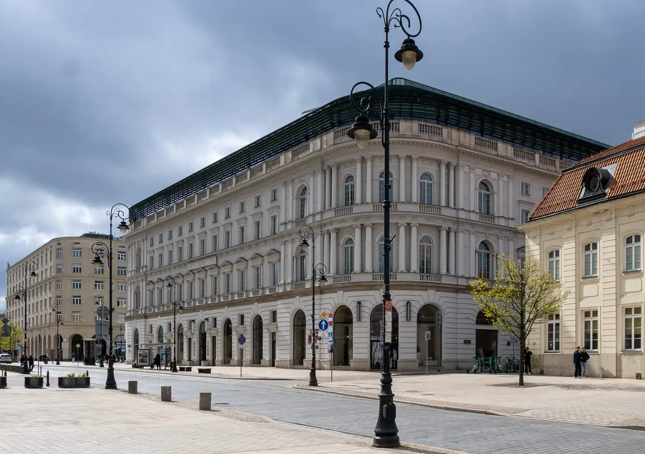 Krakowskie Przedmieście gatvė Varšuvoje su žibintais ir šviesiais istoriniais pastatais po debesuotu dangumi